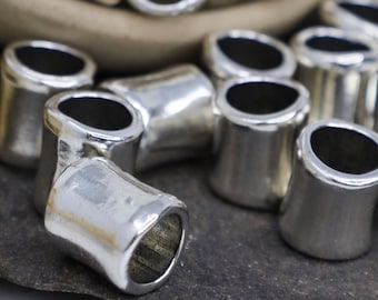 Puede incluir: Primer plano de tapones finales de metal plateado para la elaboración de joyas. Los tapones son brillantes y tienen un acabado liso y redondeado.