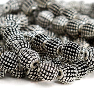 May include: Close-up of a collection of silver-coloured beads. The beads have a textured, ridged surface with a dark centre. The beads are strung together, suggesting they are for jewellery making or crafting.