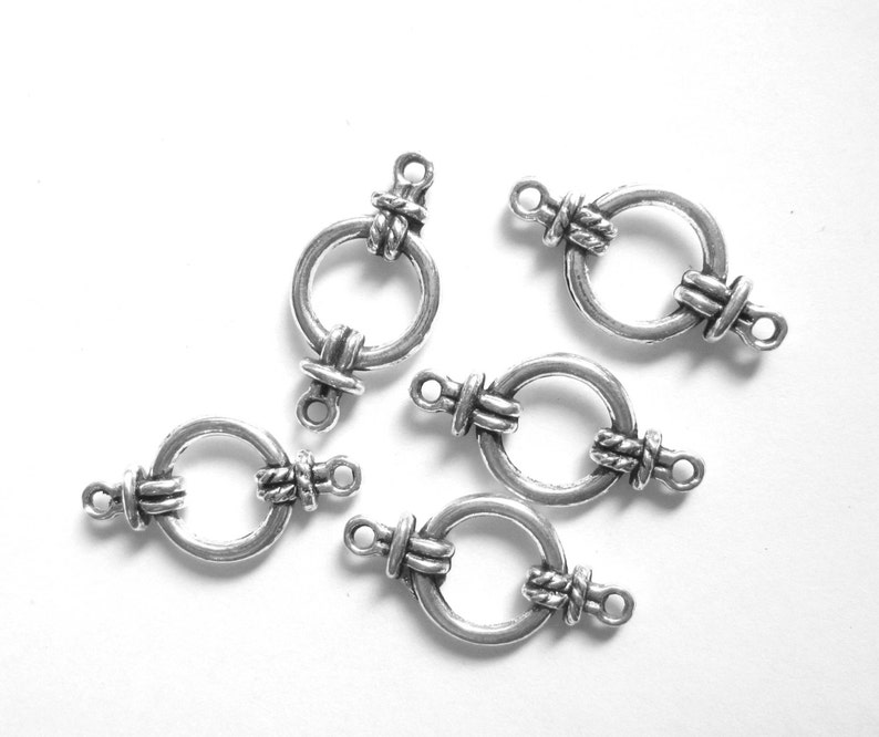 May include: Five silver-toned metal clasps with a decorative knot design. Each clasp has a circular ring and two loops for attaching to jewelry or other crafts.