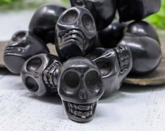 May include: A close-up of a pile of black skull-shaped beads. The beads are made of polished black stone and have intricate details.