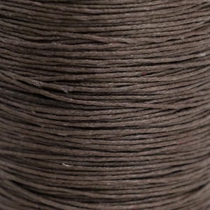 May include: Close-up of a spool of brown waxed cotton cord. The cord is tightly wound and has a smooth, even texture.