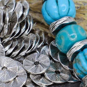 May include: A silver metal bracelet with turquoise blue beads and silver metal spacers. The bracelet is made of many small, round, silver metal pieces that are stacked on top of each other.