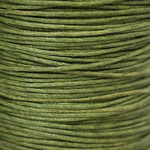 May include: Close-up of a spool of green waxed cotton cord. The cord is tightly wound and has a smooth, even texture.