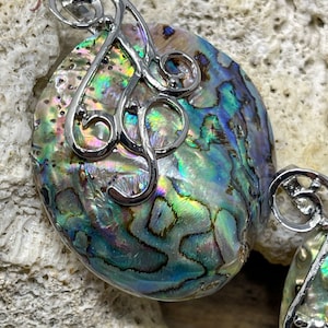 May include: A pair of iridescent abalone shell earrings with silver filigree accents. The shells are oval shaped and have a natural, organic pattern.