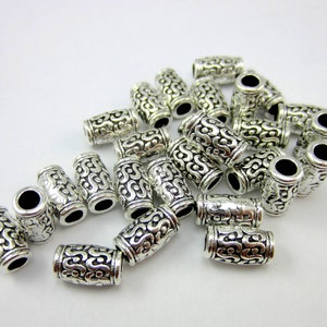 May include: A pile of silver-toned metal beads with an intricate, swirling design. The beads are cylindrical and have a smooth, polished finish.