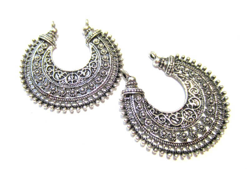 May include: Two silver filigree crescent moon shaped metal charms with a decorative design.