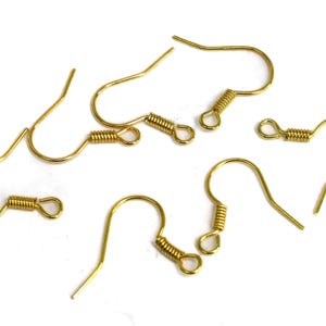 May include: Several gold-colored earring hooks are scattered on a white surface. Each hook features a curved design with a coiled spring detail near the top, and a straight, pointed end for insertion into the ear.