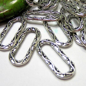 May include: Silver metal oval-shaped jump rings with a decorative design. The rings have a textured surface with small raised dots.