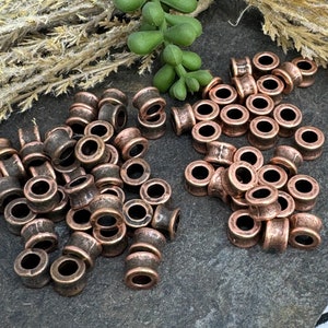 May include: A large pile of copper-colored metal beads. The beads are round with a hole in the center and have a slightly textured surface.