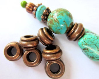 May include: Five copper-toned bead spacers with a round hole in the centre. The spacers are arranged in a pile. A turquoise and copper bead necklace is visible in the background.