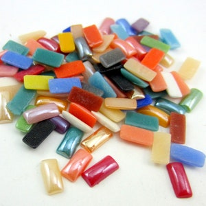 May include: A pile of colorful, rectangular glass tiles. The tiles are in various shades of red, orange, yellow, green, blue, purple, and brown. Some of the tiles have a shiny, iridescent finish.
