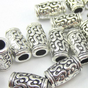 May include: Silver metal bead caps with an intricate, ornate design. The caps are cylindrical and have a smooth, polished finish.