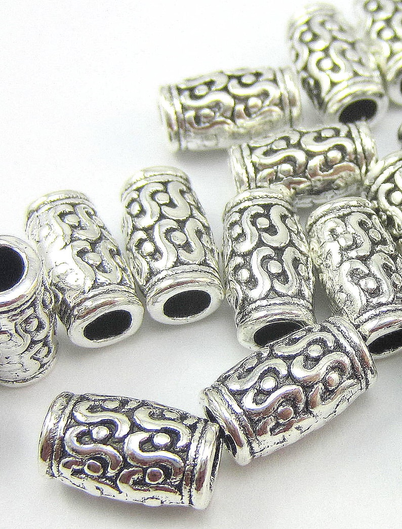 May include: Silver metal bead caps with an intricate, ornate design. The caps are cylindrical and have a smooth, polished finish.