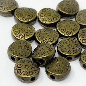 May include: A group of 12 antique gold oval-shaped beads with a decorative pattern. The beads have a hole in the center for stringing.
