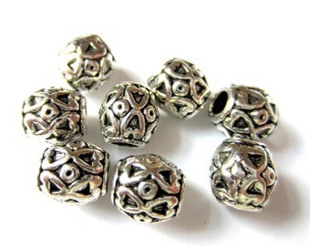 Può includere: Una collezione di perline in metallo color argento con un design traforato. Le perline hanno una forma arrotondata e geometrica con motivi a cuore e cerchio. Le perline sono sparse su uno sfondo bianco.