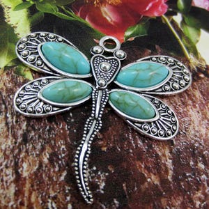 May include: Silver dragonfly pendant with turquoise stones. The dragonfly has a detailed design with a long tail and five turquoise stones.