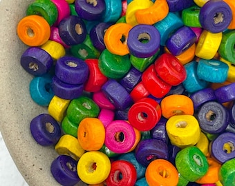 May include: A bowl filled with colorful wooden beads. The beads are round with a hole in the center and are painted in various shades of red, orange, yellow, green, blue, and purple.