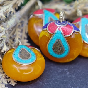 May include: Four round amber pendants with intricate turquoise, red and blue enamel designs. The pendants have a silver-toned metal bail.