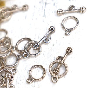 May include: A collection of silver-toned metal toggle clasps for jewelry making. Each set consists of a circular ring with a textured, rope-like pattern and a matching T-bar component featuring small decorative spheres at both ends.