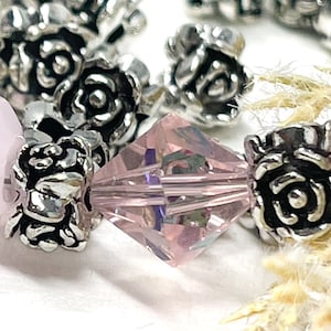 May include: Close-up of a bracelet with pink faceted beads and silver rose-shaped spacers. The beads are translucent, and the silver spacers add detail. The bracelet is set against a soft, neutral background.