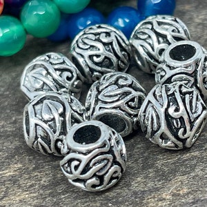 May include: A set of eight silver metal beads with an intricate floral design. The beads are round and have a hole in the center for threading.