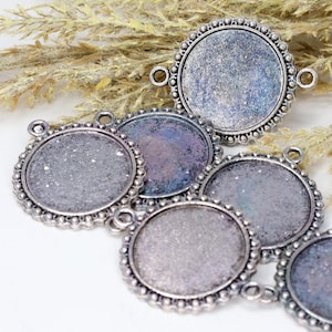 May include: A collection of silver-toned, round pendant trays with decorative beaded edges. Each tray has a circular recessed area for adding a design. The trays have small loops for attaching to a chain or other jewelry component.