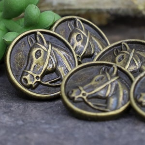 May include: A set of four antique gold-toned metal buttons featuring a horse head design. Each button has a detailed horse head with a bridle and a textured surface.