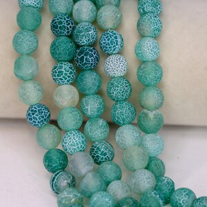 May include: Strands of round, green beads with a cracked, web-like pattern. The beads vary in shades of green, from light to dark, and are strung together. These beads are suitable for jewelry making.