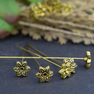 May include: Four gold-toned flower-shaped head pins with a decorative design. The pins are on a dark surface.