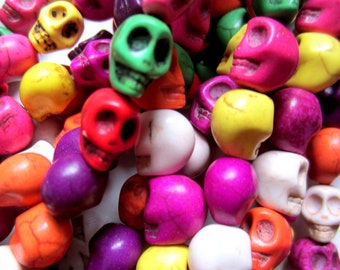 Puede incluir: Primer plano de un montón de cuentas de calaveras coloridas en varios tonos de rojo, rosa, verde, amarillo, naranja, morado y blanco. Las cuentas son pequeñas y parecen ser de piedra. Las calaveras son un tema popular.