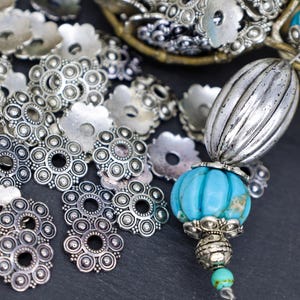 May include: A collection of silver-toned metal beads and spacers with a turquoise gemstone bead. The beads have a circular design with a central hole.