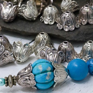 May include: A close-up of a silver metal bead with a turquoise blue center. The bead is surrounded by other silver metal beads, some of which are in the shape of a flower.