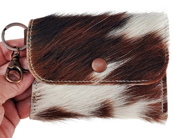 May include: A small brown and white cowhide leather keychain wallet with a metal key ring and a snap closure.