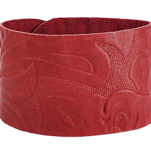 May include: A red leather cuff bracelet with an embossed floral pattern.