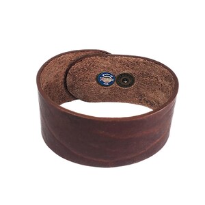 K&ouml;nnte beinhalten: Ein braunes Lederarmband mit einem Druckknopfverschluss. Das Armband hat ein "Made in USA"-Etikett auf der Innenseite.