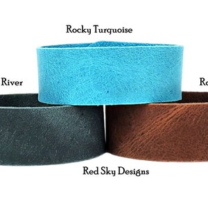 K&ouml;nnte beinhalten: Drei Lederarmb&auml;nder in verschiedenen Farben: T&uuml;rkis, Dunkelblau und Braun. Die Armb&auml;nder sind &uuml;bereinander gestapelt. Der Text "Rocky Turquoise", "Rocky River" und "Rocky Road" steht &uuml;ber jedem Armband. Der Text "Red Sky Designs" steht unter den Armb&auml;ndern.