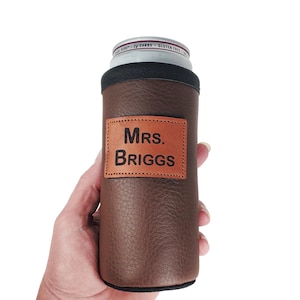 May include: Brown faux leather can cooler with a brown leather patch that says "Mrs. BRIGGS" in black lettering.