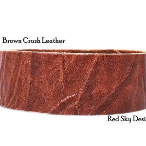 K&ouml;nnte beinhalten: Nahaufnahme eines braunen Lederriemens mit strukturierter Oberfl&auml;che. Der Riemen ist mit "Brown Crush Leather" und "Red Sky Designs" beschriftet.