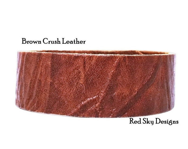 K&ouml;nnte beinhalten: Nahaufnahme eines braunen Lederriemens mit strukturierter Oberfl&auml;che. Der Riemen ist mit "Brown Crush Leather" und "Red Sky Designs" beschriftet.