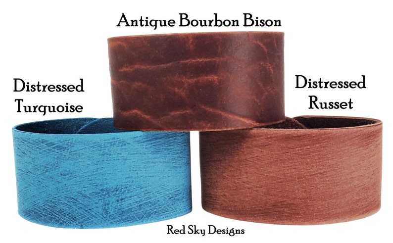 K&ouml;nnte beinhalten: Drei Lederarmb&auml;nder in verschiedenen Farben und Texturen. Das obere Armband ist braun mit einem abgenutzten Look und ist mit "Antique Bourbon Bison" beschriftet. Das mittlere Armband ist blau mit einem abgenutzten Look und ist mit "Distressed Turquoise" beschriftet. Das untere Armband ist rotbraun mit einem abgenutzten Look und ist mit "Distressed Russet" beschriftet.