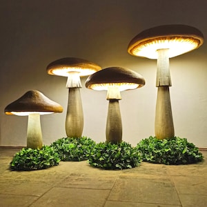 以下が含まれることがあります： 緑の葉っぱの上に置かれた、光る電球が付いたキノコの形をしたランプが4つあります。ランプは薄い茶色の素材で作られており、本物のキノコのように見えます。