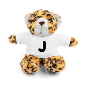 May include: A plush leopard-print teddy bear with a white t-shirt featuring a black letter "J". The bear has a tan nose, white accents, and orange and black spots. The bear is sitting with its arms outstretched.