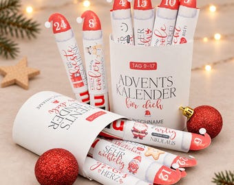 May include: An advent calendar set featuring white cylindrical tubes with red Santa hat caps, each numbered and printed with German text. The tubes are arranged in two white containers labeled Advents Kalender für dich.