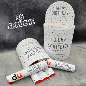 Könnte beinhalten: Ein zylindrischer weißer Behälter mit bunten Punkten und dem Text "HAPPY BIRTHDAY to you" sowie "Für DICH soll es KONFETTI regnen". Daneben liegen mehrere kleine weiße zylindrische Gegenstände mit roten Enden, die Texte wie "GLÜCK der Welt" und "GEBURTSTAG" tragen.