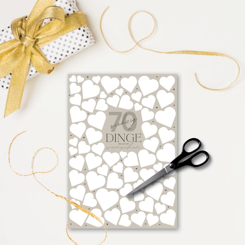 May include: A gift wrapped in white paper with black polka dots and a gold ribbon. A greeting card with white hearts and the text "70 Dinge die wir uns w&uuml;nschen" is next to a pair of black scissors and gold ribbon.