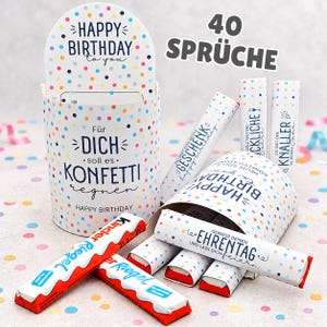 Op de afbeelding: Een cilindervormige witte houder met kleurrijke stippen en de tekst "HAPPY BIRTHDAY to you" en "Für DICH soll es KONFETTI regnen". Het wordt omringd door diverse kleine witte buisjes met verjaardagsteksten en twee Kinder Riegel chocoladerepen.