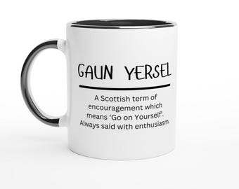 May include: White ceramic coffee mug with a black rim and handle. The mug has black text that reads "GAUN YERSEL" and a definition of the phrase, which is a Scottish term of encouragement meaning "Go on Yourself."