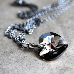 May include: A silver chain necklace with a large, faceted, black heart-shaped crystal pendant.