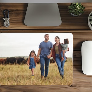 May include: A family of four walks through a field with cows in the background. The parents are holding hands and the two children are walking beside them. The family is wearing casual clothing and smiling.