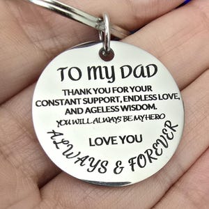 May include: A silver-colored, round keychain pendant with the inscription "TO MY DAD" and a heartfelt message. The text includes phrases like "THANK YOU FOR YOUR CONSTANT SUPPORT" and "ALWAYS & FOREVER."